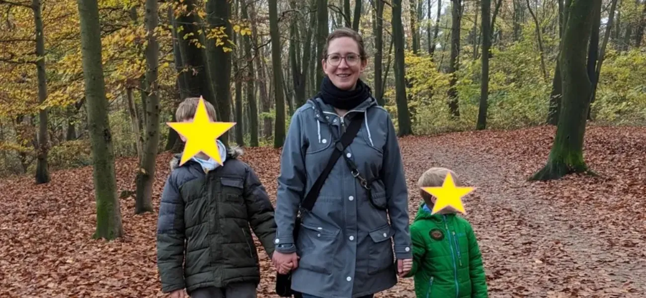 Gina steht mit ihren Kindern auf einem Waldweg und schaut in die Kamera