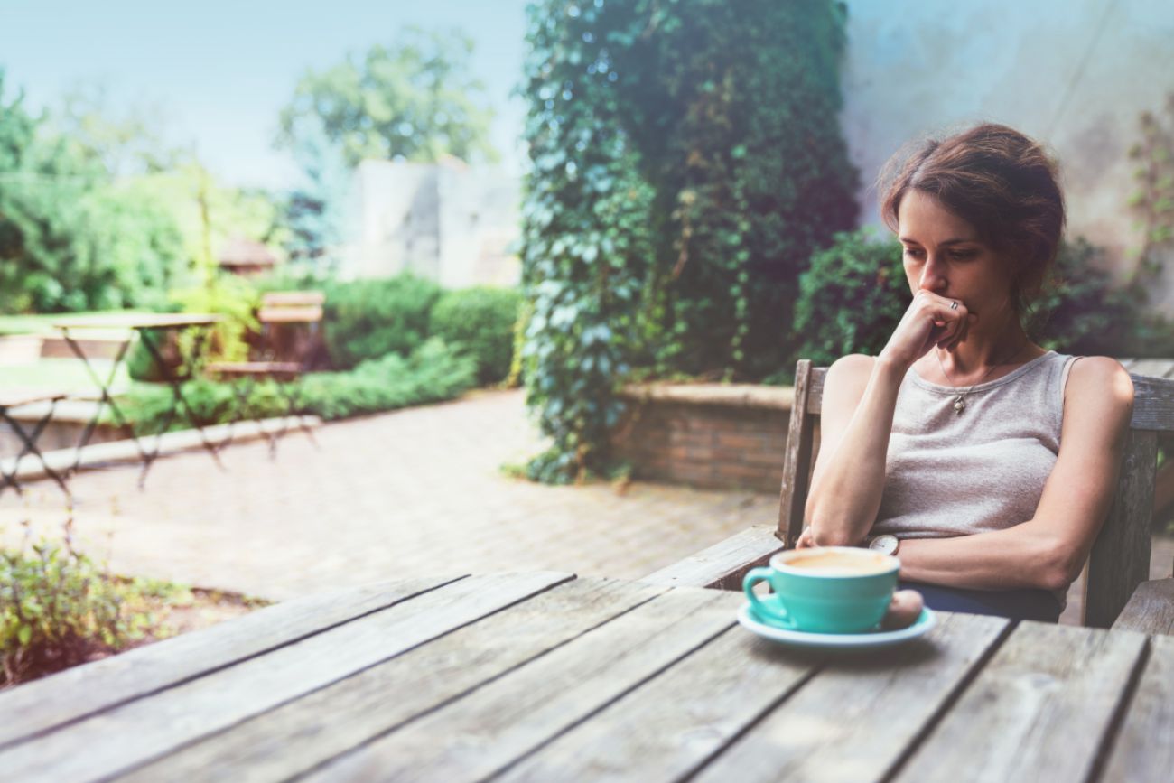 Nachdenkliche Frau im Garten vor einem Kaffee