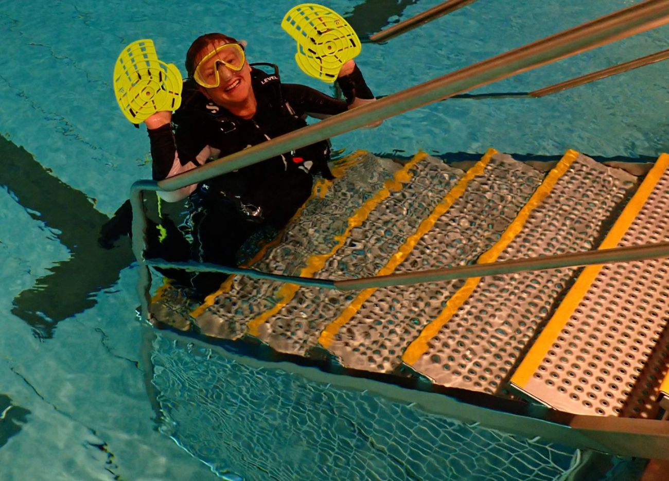Nicole im Schwimmbecken stehend und die Handpaddles hochhaltend