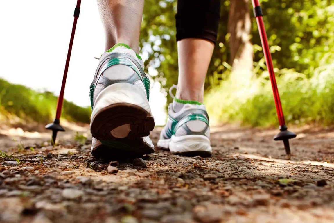 Eine Frau geht mit Nordic-Walking-Stöcken einen Weg entlang.