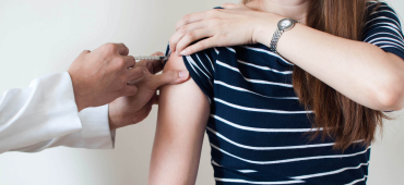 Ein Arzt injiziert einen Impfstoff in den Oberarm einer jungen Frau