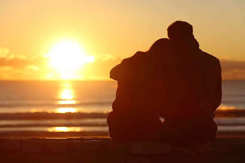 Arm in Arm am Strand dem Sonnenuntergang zuschauen