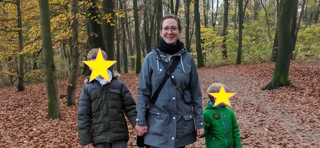 Gina steht mit ihren Kindern auf einem Waldweg und schaut in die Kamera